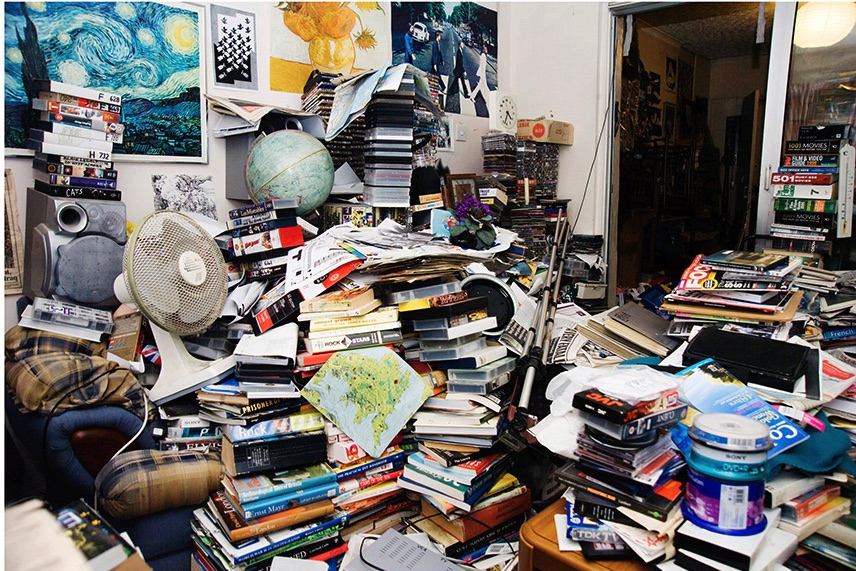 Stacks of books, movies, papers, and hobby items in a crowded Ferndale room